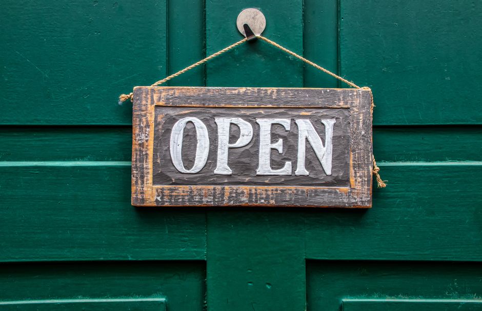 A vintage wooden open sign hanging on a rustic green door